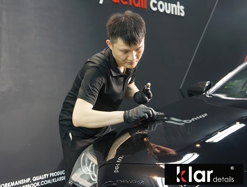 Technician applying coating to black car hood
