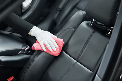 White-gloved hands cleaning a black car seat with a pink cloth