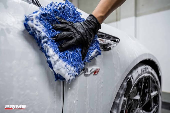 Gloved hand washing a white car with a blue microfiber mitt